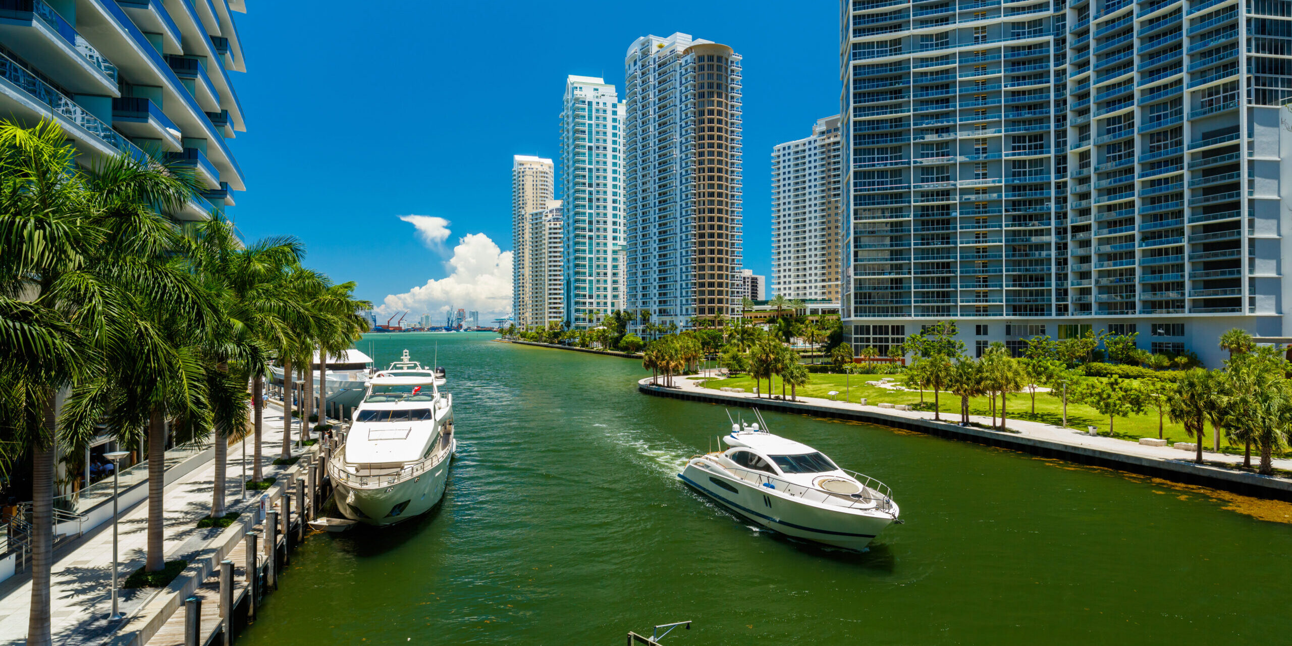 Image of yachts in the Miami river docked alongside the shore and crusing