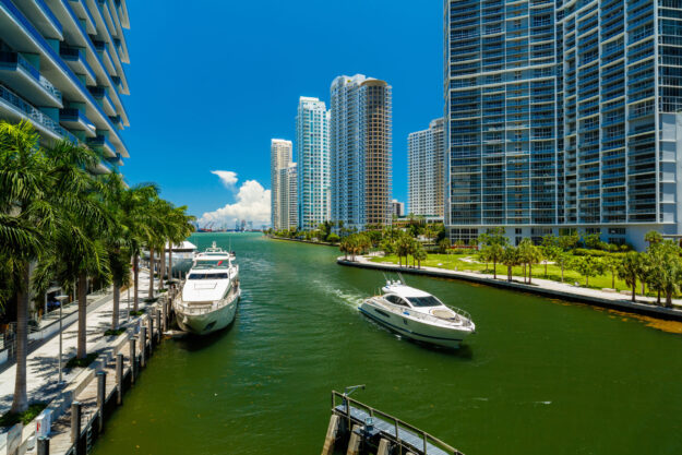 Image of yachts in the Miami river docked alongside the shore and crusing